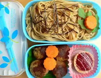 A photograph of a blue bento box (Japanese lunchbox) with long soba noodles in the top
  comparment and small, round cakes in a compartment below.  The noodles and cakes are fully separated.
  The long noodles are tangled together while the cakes are beautifully arranged.  A set of chopsticks
  rest on the left side of the bento box.